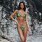 Woman in a green and brown patterned bikini standing against a rocky background