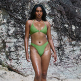 Woman in a green bikini standing against a rocky background